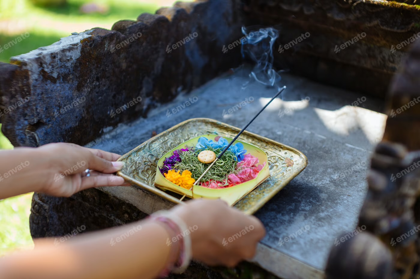 Hands placing a flower offering and incense on a stone shrine